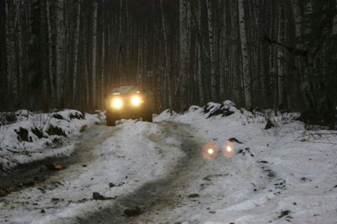 2003 Jeep TJ - A red SUV navigates a snow-covered road through a dark forest, its headlights cutting through the night.