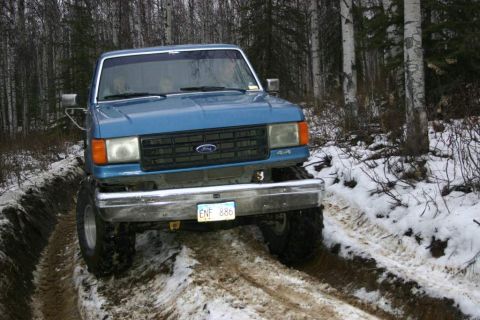 2003 Jeep TJ - This blue Ford pickup truck is navigating a challenging off-road trail in a wooded area during winter.