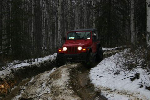 2003 Jeep TJ - A red Jeep TJ navigates a challenging muddy and snowy path in a wooded area.
