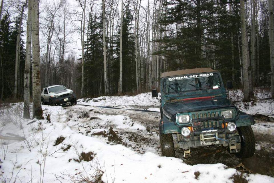 Green Jeep Wrangler with winch stuck in mud and snow, white SUV in background also stuck