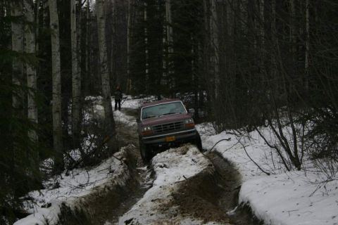 2003 Jeep TJ - A maroon pickup truck navigates a challenging off-road trail covered in snow and mud.