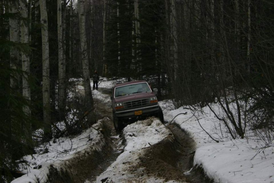 Maroon pickup truck driving on a snowy, muddy trail in a forest