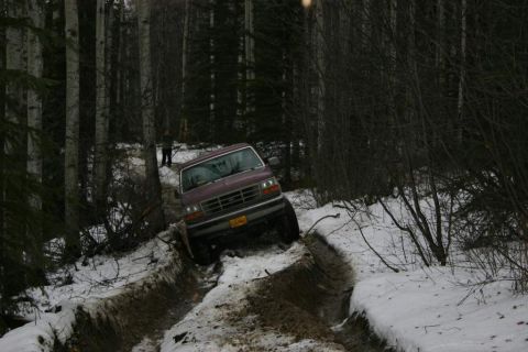2003 Jeep TJ - A maroon 1992 Ford Bronco navigates a challenging snowy and muddy path through a forest.