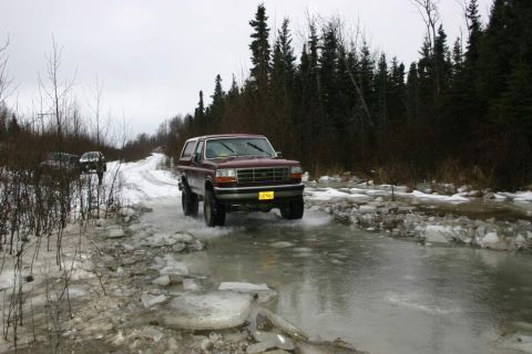 2003 Jeep TJ - Ford Bronco navigates an icy road with another vehicle following in the background.