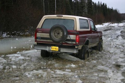 2003 Jeep TJ - A Ford Bronco navigates a partially frozen, icy road surrounded by trees.