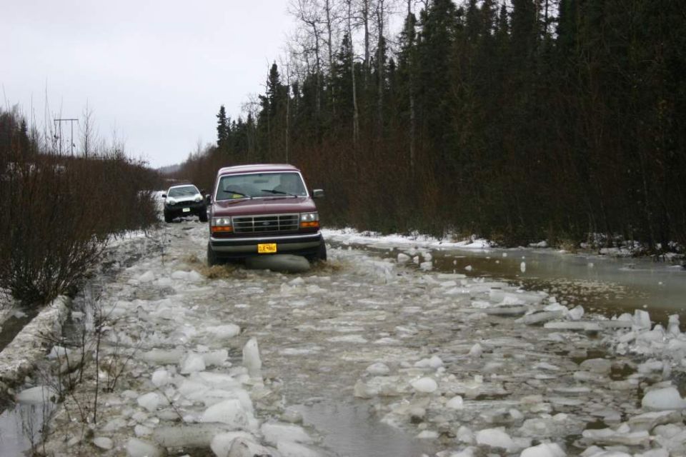 Maroon SUV driving through icy water, front view. License plate is yellow