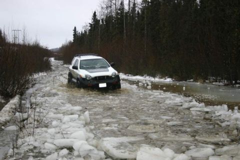 2003 Jeep TJ - A white SUV navigates a partially frozen and flooded road surrounded by dense trees.