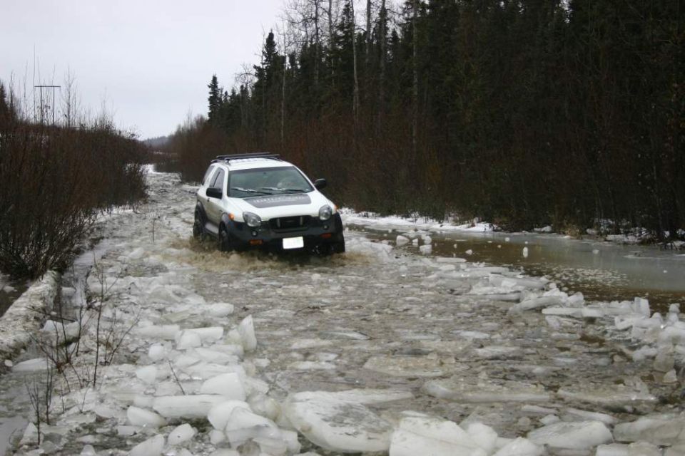 White SUV driving through a flooded, icy road with trees in the background