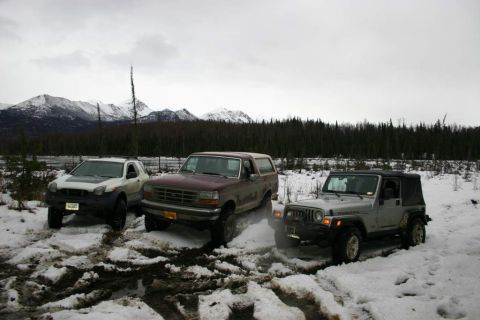 2003 Jeep TJ - Three SUVs navigate snowy terrain with mountains and forest visible.