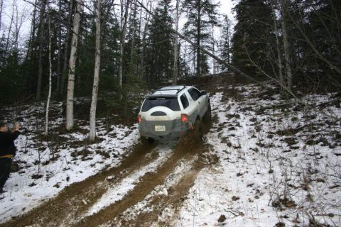 2003 Jeep TJ - A white SUV navigates a muddy, snow-covered incline in a wooded area.