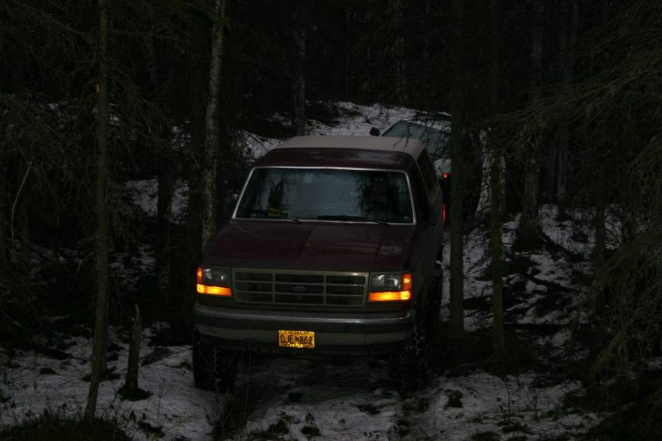 Maroon Ford Bronco with a light-colored top parked in a snowy forest. Another vehicle is visible behind it