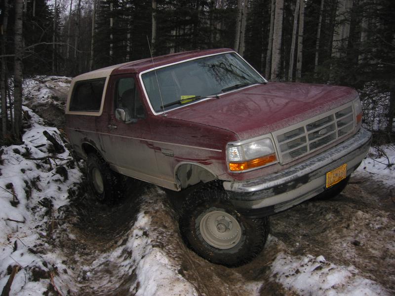 1993 Ford Bronco navigating a muddy, snowy trail in a forest