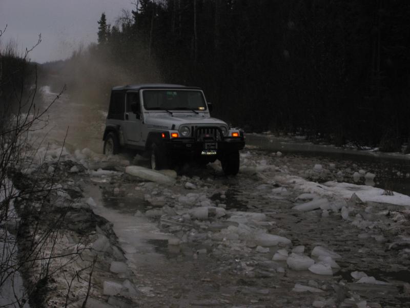 Silver Jeep Wrangler driving through ice and slush on a dirt road