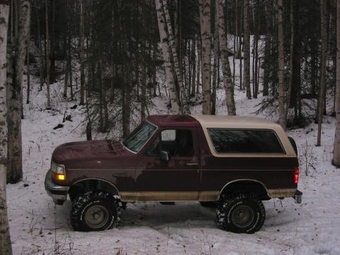 1993 Ford Bronco - A lifted Ford Bronco sits in a snow-covered wooded area during winter.