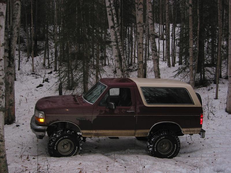 Maroon Ford Bronco with tan top parked in a snowy forest