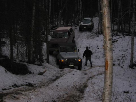 1993 Ford Bronco - Multiple SUVs navigate a snowy, wooded path in a winter scene.