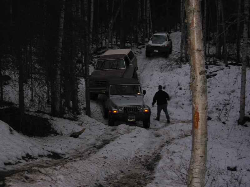 Three SUVs on a snowy forest trail, one is a dark red Bronco-like vehicle