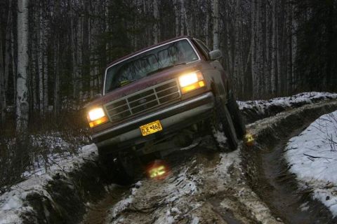 1993 Ford Bronco - A maroon Ford Bronco navigates a challenging muddy and snowy off-road trail.