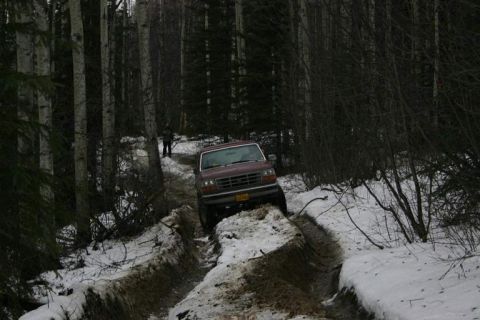 1993 Ford Bronco - A maroon 1992 Ford Bronco navigates a muddy and snowy path through a dense forest.