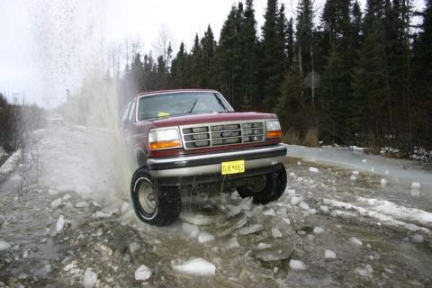 1993 Ford Bronco - A red 1993 Ford Bronco splashes through icy water on a wooded road.