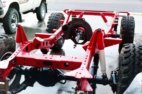 1976 Toyota Land Cruiser - The red painted frame and suspension of a vehicle sits on a wet surface, with another vehicle partially visible in the background.