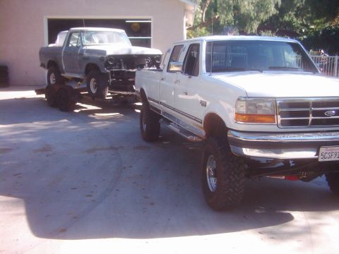1978 Ford Bronco - A white pickup truck tows a gray pickup truck on a trailer, possibly for restoration or transport.