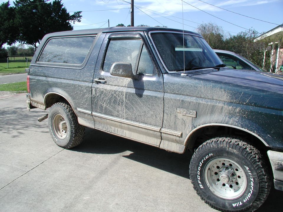 Side view of a dark-colored 1993 Ford Bronco covered in mud splatters. It has BFGoodrich All-Terrain tires