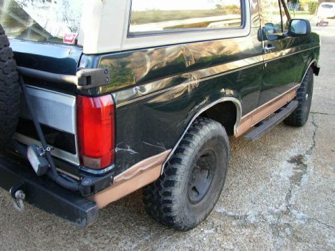 1995 Ford Bronco - Rear view of a 1995 Ford Bronco, showing its dark green paint, tan stripe, and spare tire.