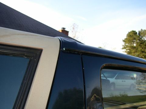 1995 Ford Bronco - The side of an SUV shows some damage to the roofline, with a minivan visible in the reflection.