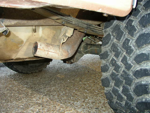 Close-up of a vehicle's rear axle, leaf springs, and exhaust pipe, with a large tire tread visible