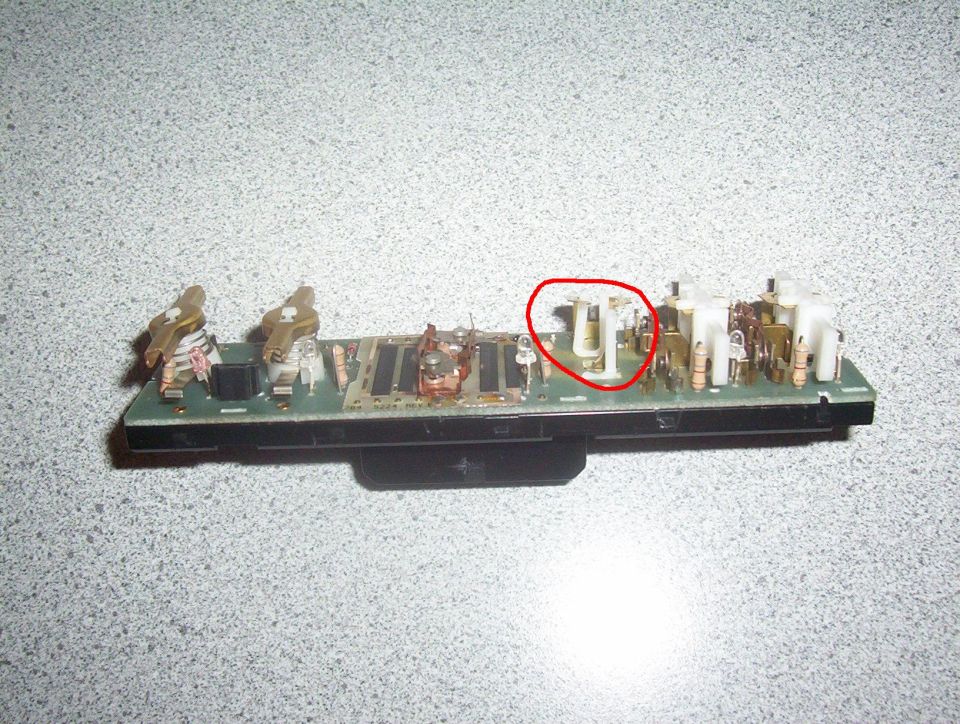 Circuit board with white plastic components and metal connectors, red circle highlighting a component