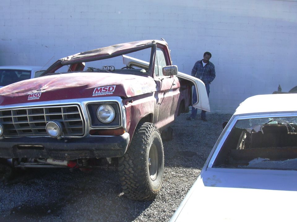 Wrecked maroon 1970s Ford 4x4 with crushed roof and MSD decals in gravel lot
