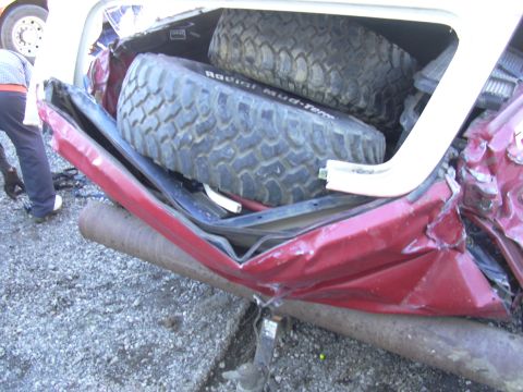 1978 Ford Bronco - The rear of a red SUV is heavily damaged, with two spare tires visible inside the cargo area.