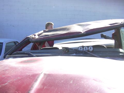 1978 Ford Bronco - A person is visible through the damaged roof of a red SUV, with another vehicle behind it.