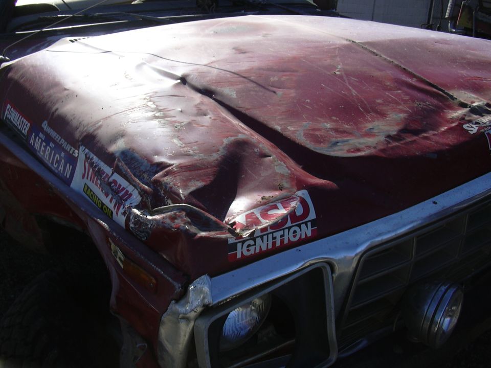 Red 1978 Ford Bronco with heavily damaged hood and fender, racing decals