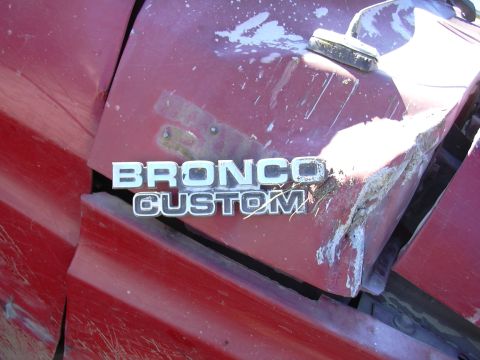 1978 Ford Bronco - Close-up of a damaged red fender with a BRONCO CUSTOM emblem, likely from a 1978 Ford Bronco.