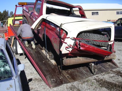 1978 Ford Bronco - A severely damaged red and white pickup truck is being loaded onto a tow truck, with a spare tire visible in the rear cargo area.