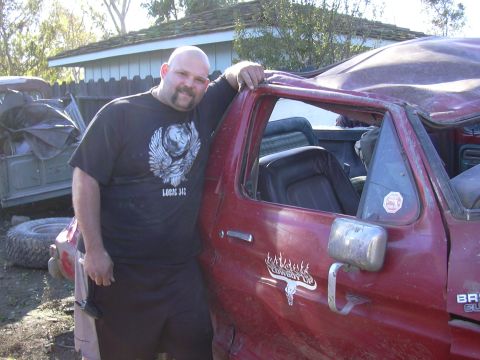1978 Ford Bronco - A man poses next to a heavily damaged red 1978 Ford Bronco, showing the side view of the vehicle.