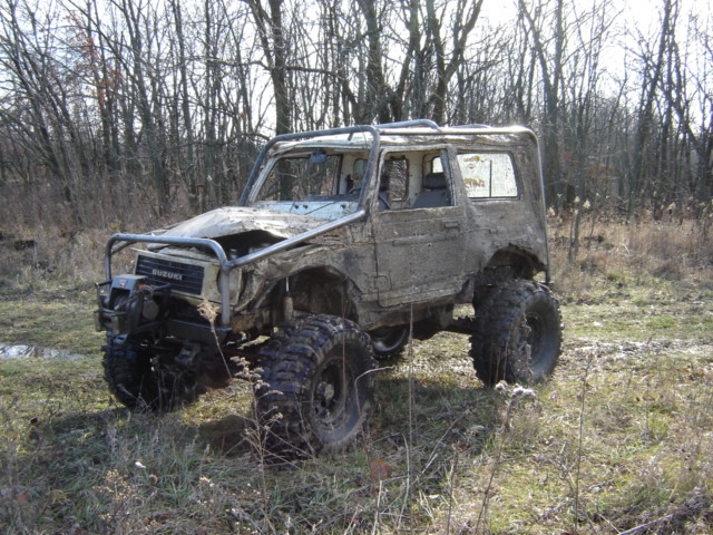 Mud-covered Suzuki with large tires and roll cage, front view