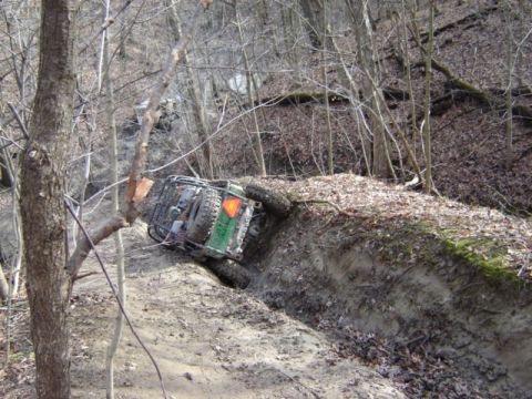 1992 Ford Bronco - An off-road vehicle navigates a challenging, muddy trail in a wooded area.