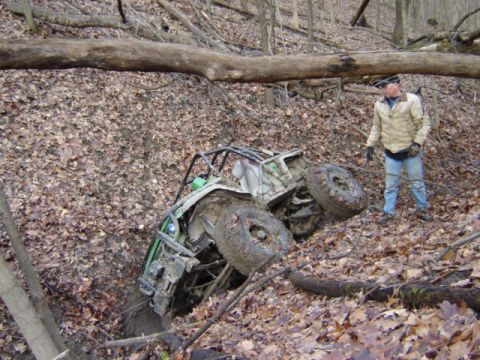 1992 Ford Bronco - A person observes an off-road vehicle that has become stuck in a muddy ditch surrounded by fallen leaves and trees.
