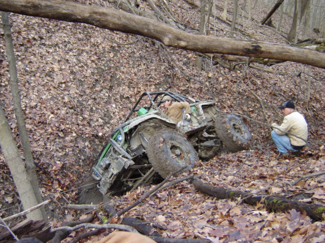 Off-road buggy stuck in mud on a wooded hillside with a person watching