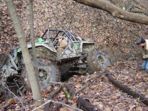 1992 Ford Bronco - An off-road vehicle is stuck in a wooded area, its tires deep in mud and debris.