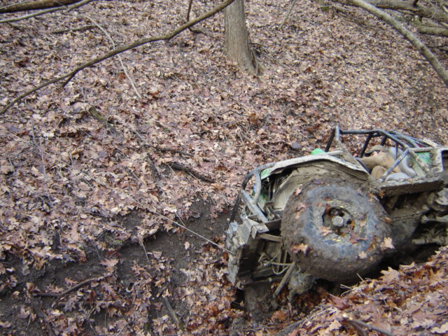 Off-road buggy with roll cage stuck in a muddy ditch covered in leaves