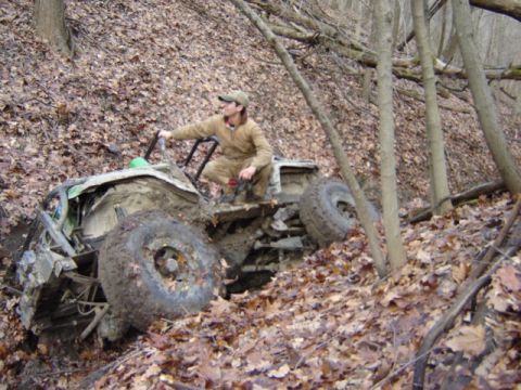 1992 Ford Bronco - An off-road vehicle is stuck in a wooded area, with a person observing its predicament.