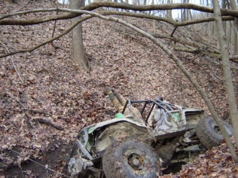 1992 Ford Bronco - Off-road buggy with roll cage stuck in a wooded ditch, driver's legs visible.