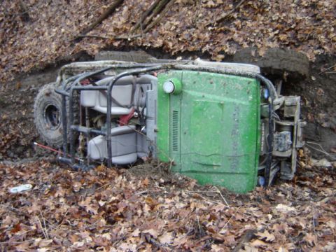 1992 Ford Bronco - An overturned green off-road vehicle lies in a muddy ditch surrounded by fallen leaves.