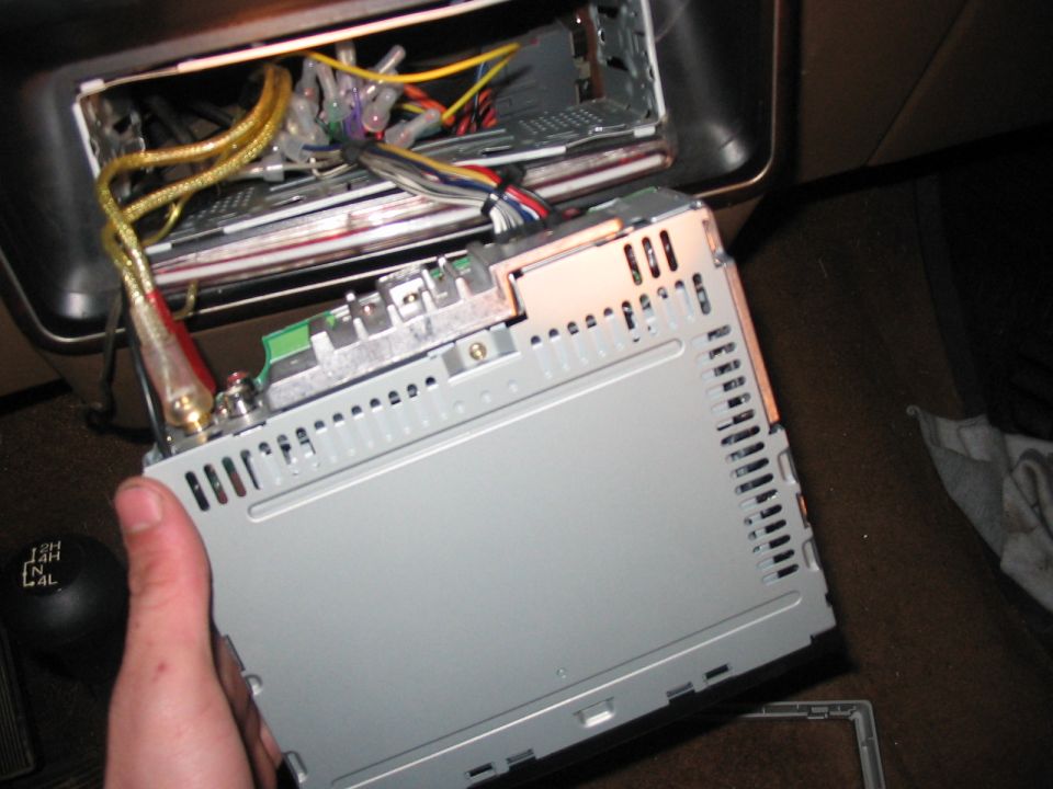 Hand holding car stereo being installed in dash, wires visible