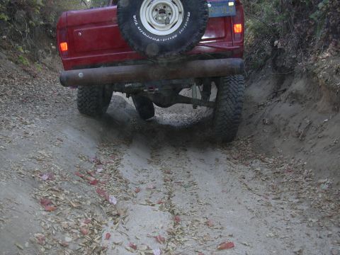 1978 Ford Bronco - The rear of a red 1978 Ford Bronco navigates a dirt path with a spare tire mounted externally.