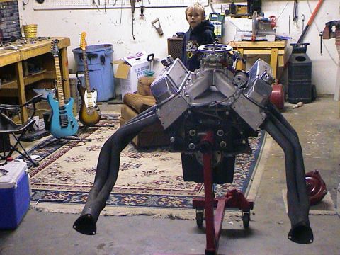 1979 Ford Bronco - A V8 engine is displayed on a stand in a cluttered garage, with musical instruments visible.